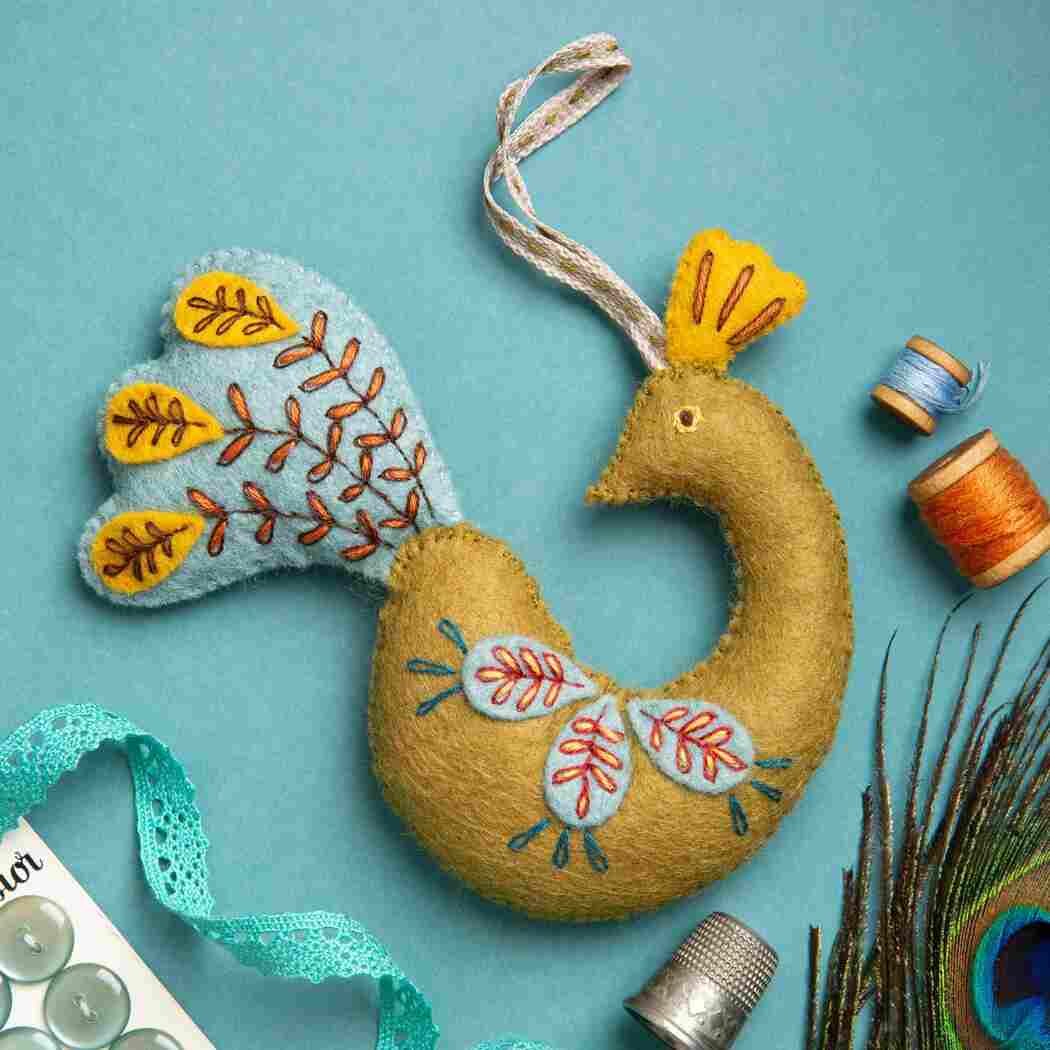 Decorative peacock feather ornament with embroidery on a teal background.
