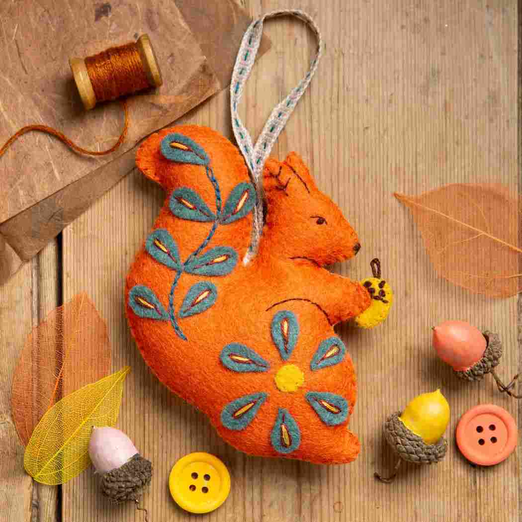 decorative felt squirrel holding an acorn on a solid wood background with scattered acorns.