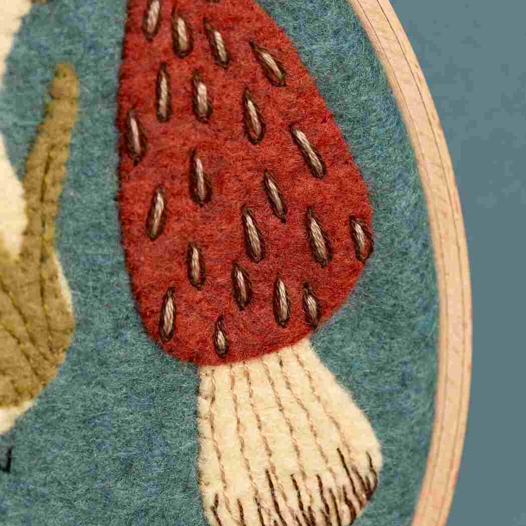 Embroidered felt mushroom with a red cap and beige stem on a blue felt background.