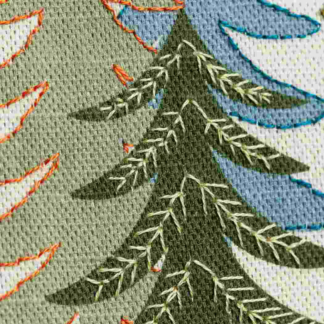 Close up of fir tree design on a linen fabric background with hand embroidered embellishments