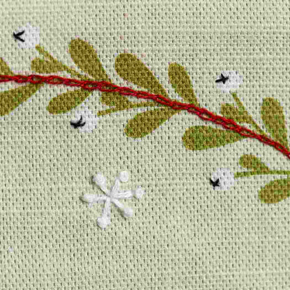 Close up of foliage design on a linen fabric background with hand embroidered embellishments
