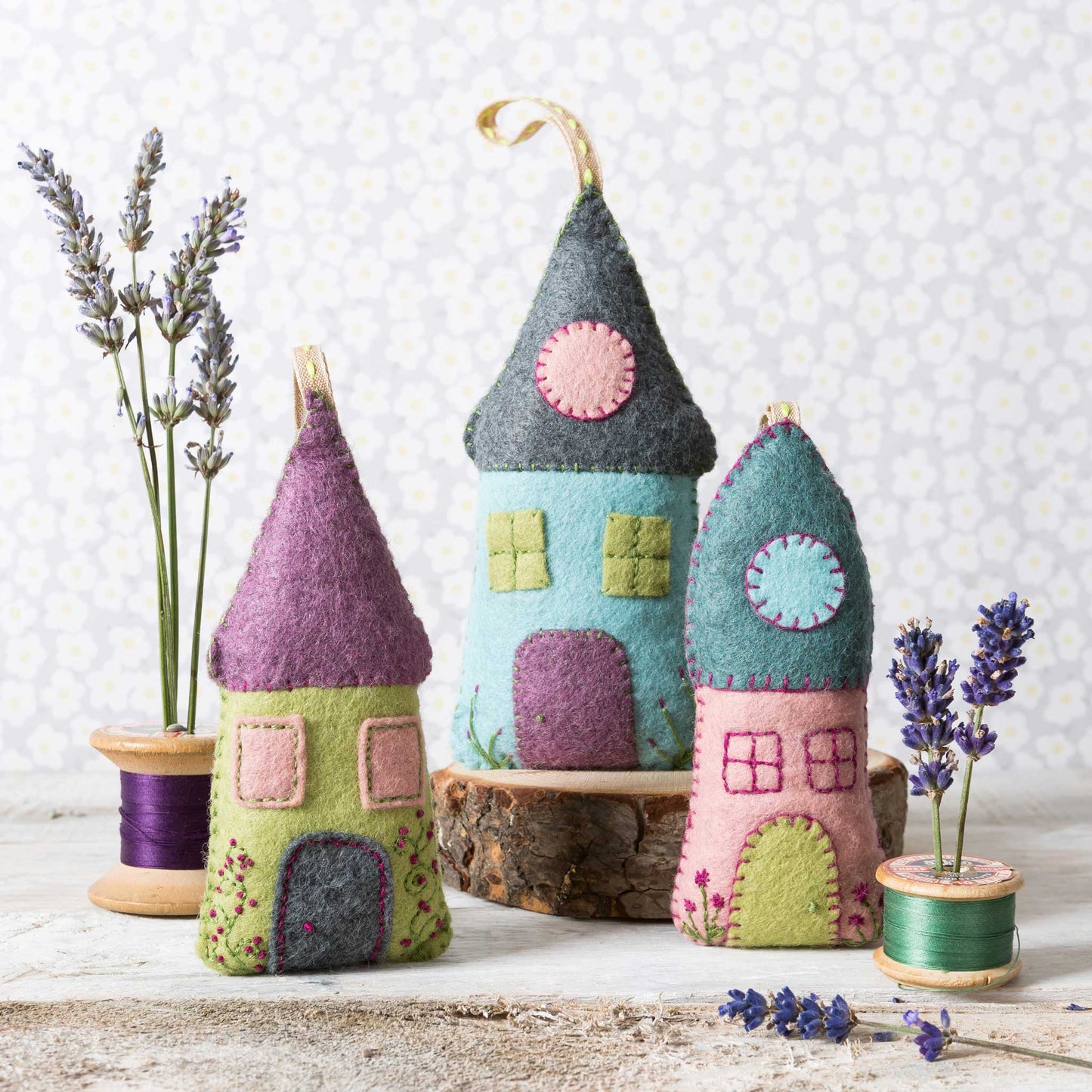 Colorful felt house ornaments on a wooden surface with lavender and spools of thread.