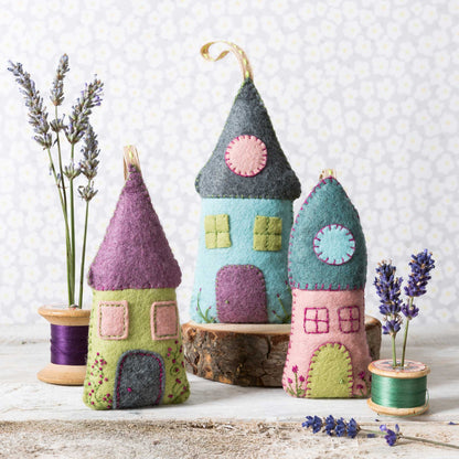 Colorful felt house ornaments on a wooden surface with lavender and spools of thread.