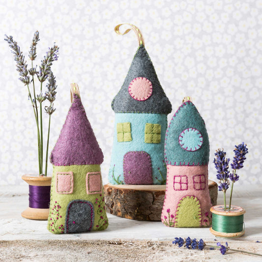 Colorful felt house ornaments on a wooden surface with lavender and spools of thread.