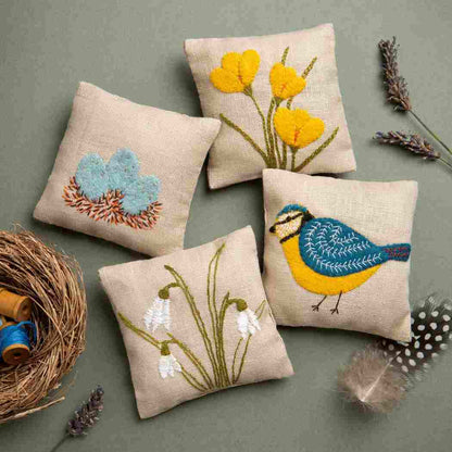 Decorative pillows with embroidered designs of flowers and a bird on a gray background.