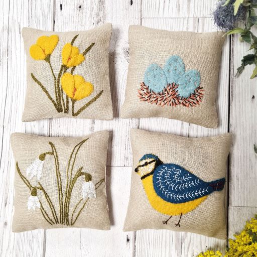 Four embroidered pillows with floral, bird, and nature-themed designs on a wooden surface. 