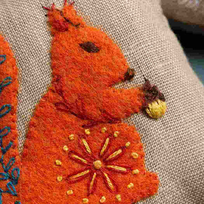 Embroidered orange squirrel with gold details on a fabric background