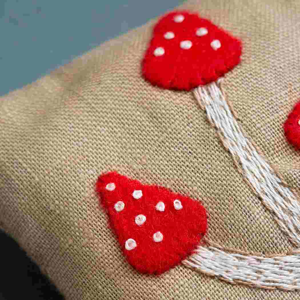 up close of embroidered red toadstool with long stocks on natural beige fabric.