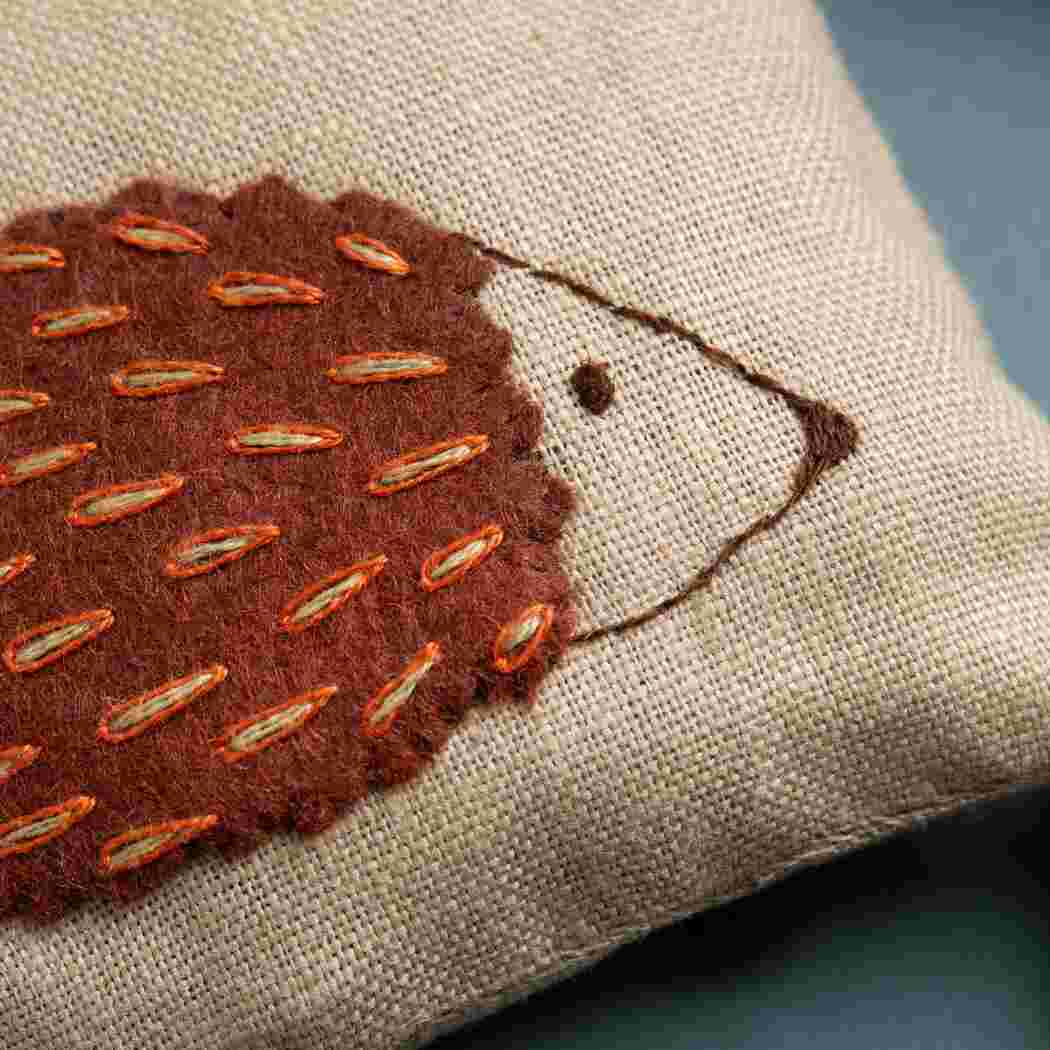 up close of brown hedgehog with stitched details on natural beige background. 