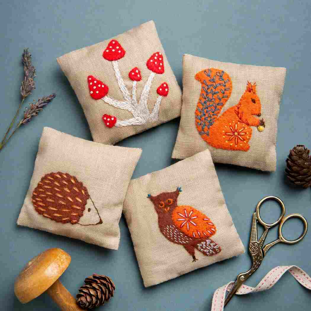 Four embroidered cushions with animal designs on a blue background, accompanied by scissors and lavender.
