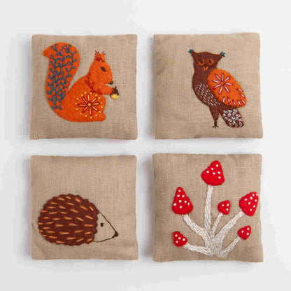 Four embroidered lavender filled cushions with animals and plants on a beige background