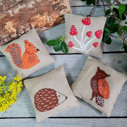 Four embroidered pillows with animal designs on a wooden surface.
