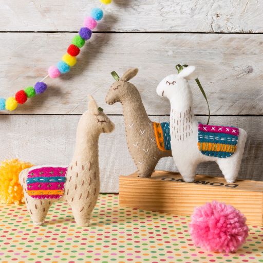Three plush llamas with colorful patterns on a wooden surface with decorative elements.