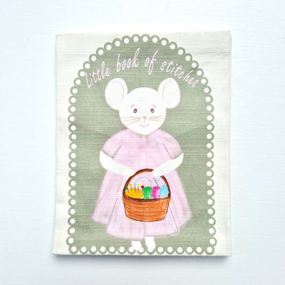 front of fabric book with the title, little book of stitches with a mouse in a pink dress holding a basket of crafts.
