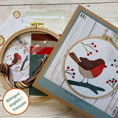 Embroidery hoop kit with robin design on a wooden surface, the kit contents of instructions, hoop, felt and threads are displayed beside the box.