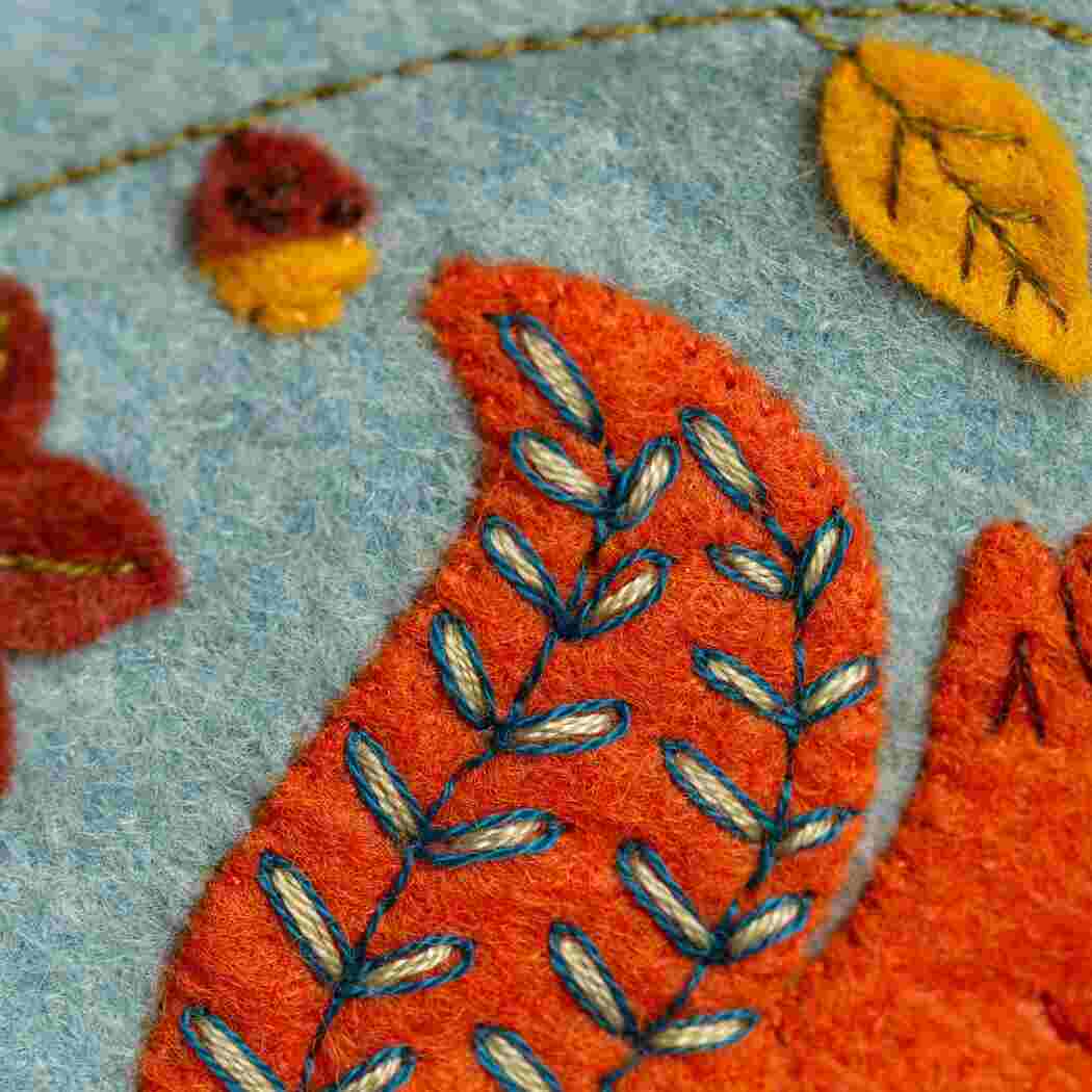 Close-up of embroidered felt fabric with orange squirrel tail and some leaves on a blue background