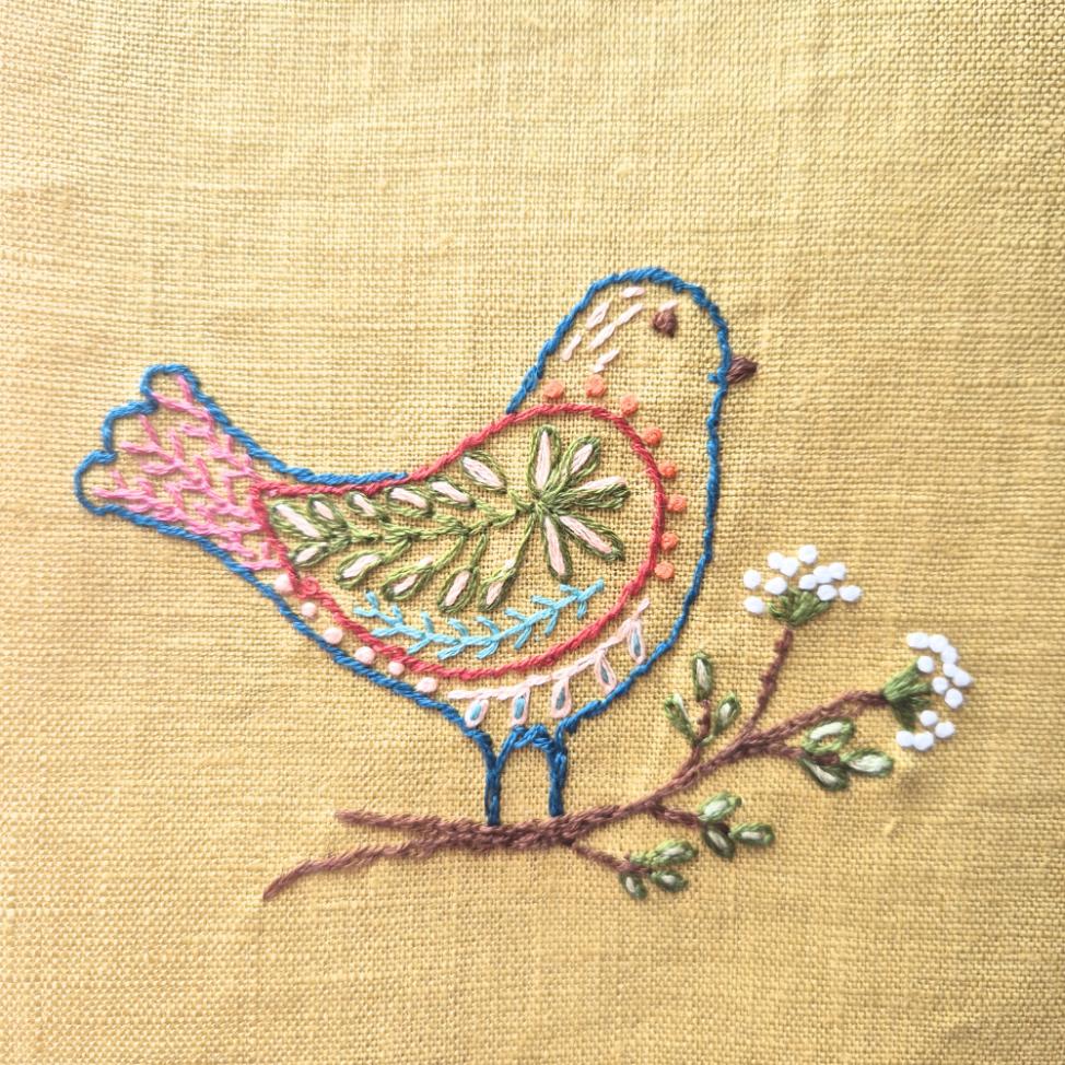 embroidered bird on a branch from the folk birds stick and stitch pack on light yellow fabric.
