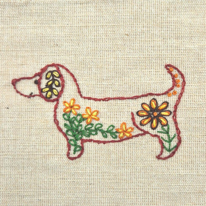 Embroidered dachshund  outlined in red design on fabric with floral patterns.