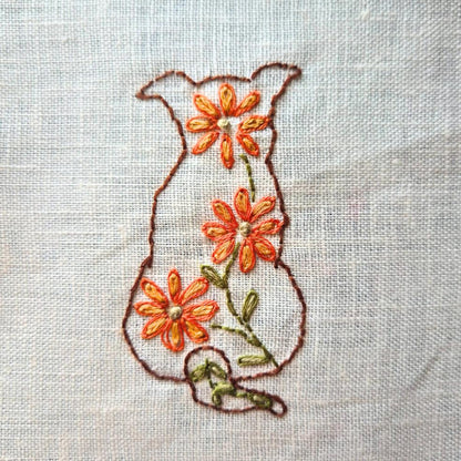 embroidered dog from behind  outlined in brown with orange flowers  on textured linen. 