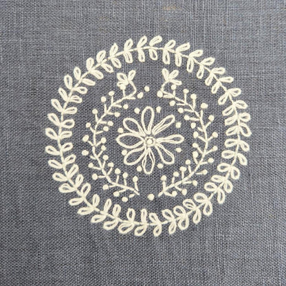 Decorative white floral embroidered pattern on a grey fabric background