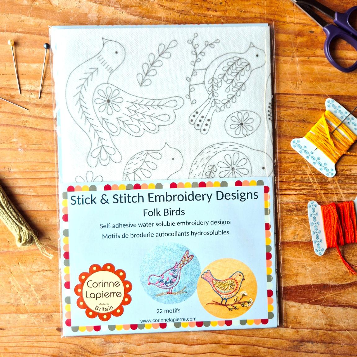 pack of folk birds embroidery designs on a wooden backdrop and an array embroidery accessories dressing the scene on a wooden surface.