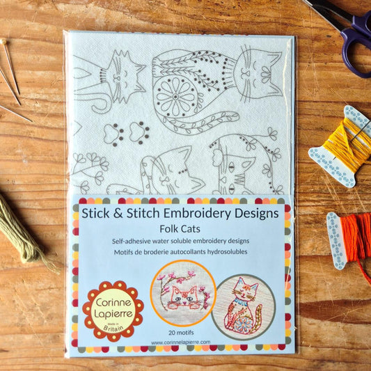 pack of embroidery stick and stitch folk cats designs. surrounded by embroidery items on a wooden surface.