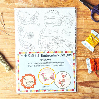 Packaging of Stick & Stitch Embroidery Designs for Folk Dogs on a wooden surface with embroidery materials.
