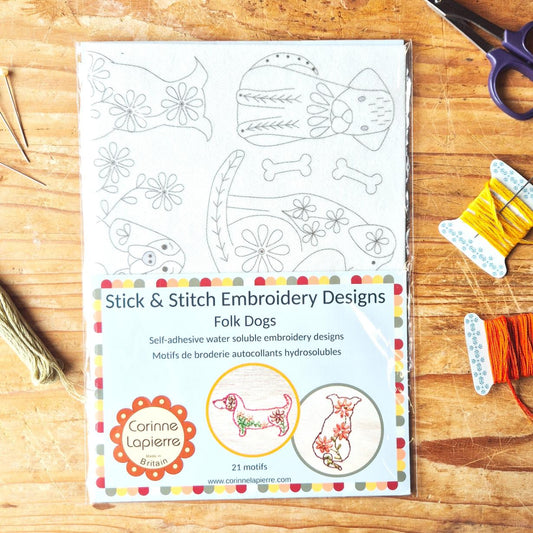 Packaging of Stick & Stitch Embroidery Designs for Folk Dogs on a wooden surface with embroidery materials.