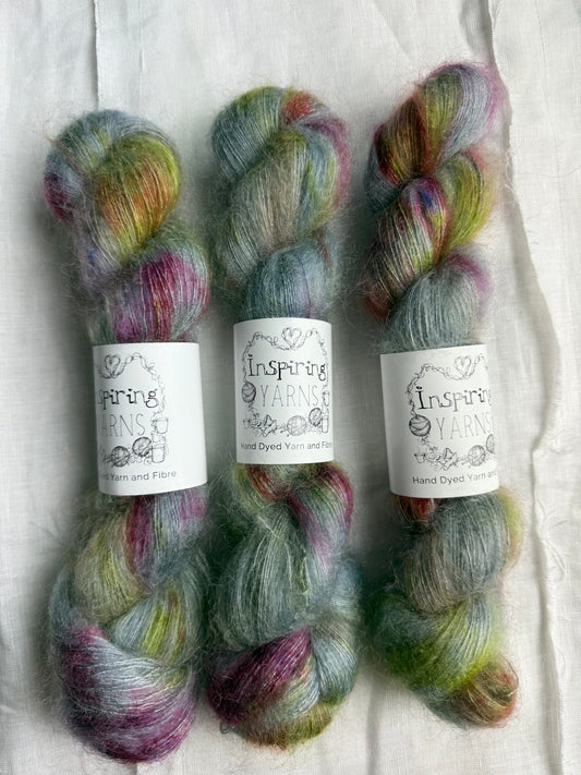 Three skeins of yarn with blueish gray tones with reds greens and browns speckled through labels on a white background.