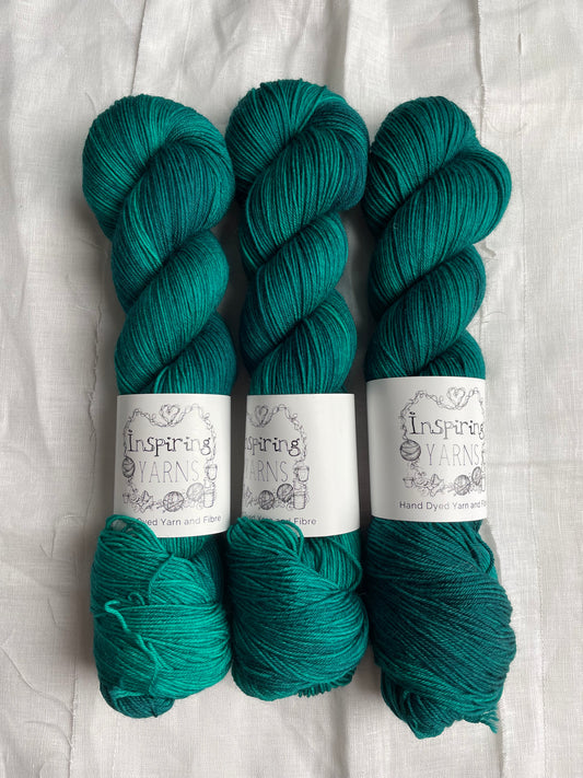 Three skeins of Merino Smooth Sock yarn hand dyed in a tonal jade green colourway and labelled Inspiring Yarns on a white linen background.