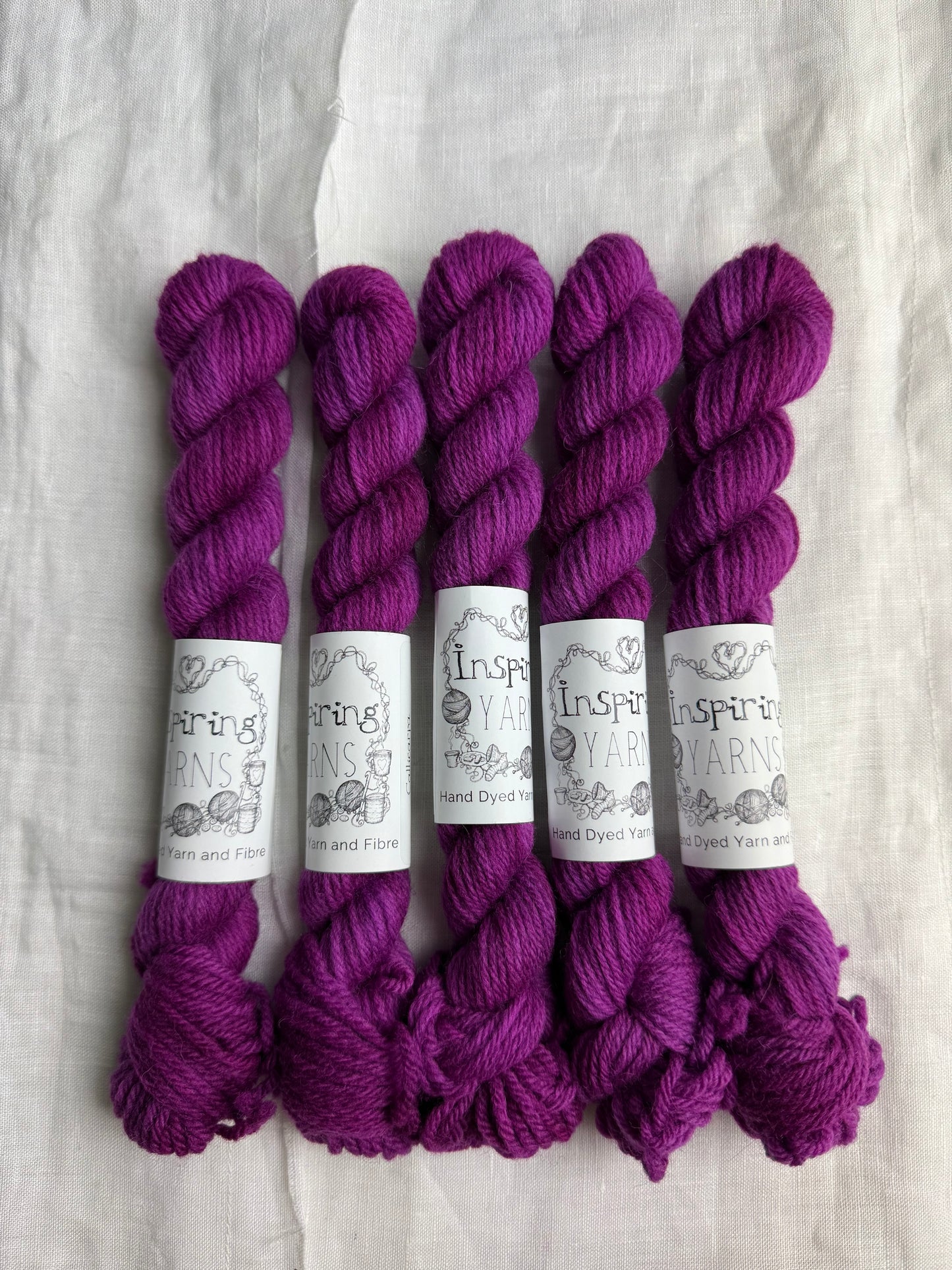 Five skeins of fuchsia tonal yarn labelled Inspiring Yarns on a white background