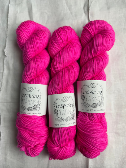three skeins of intense neon pink yarn with inspiring yarns label on a white background.
