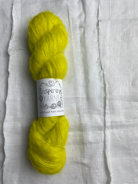 A skein of tonal acid yellow coloured hand dyed fluffy Alpaca Silk Lace yarn labelled Inspiring Yarns on a white linen background. 