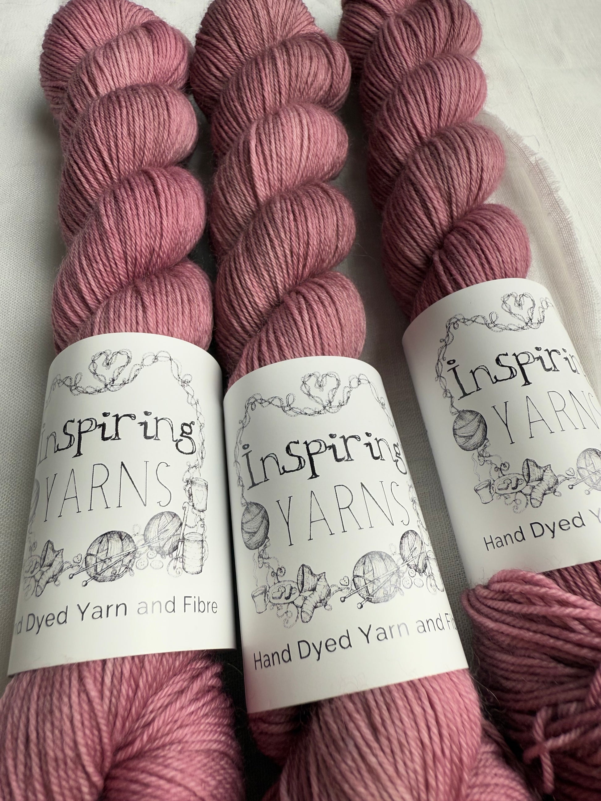 close up of three skeins of dusty  pink yarn with inspiring yarns  labels on a white background.