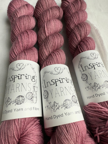 close up of three skeins of dusty  pink yarn with inspiring yarns  labels on a white background.