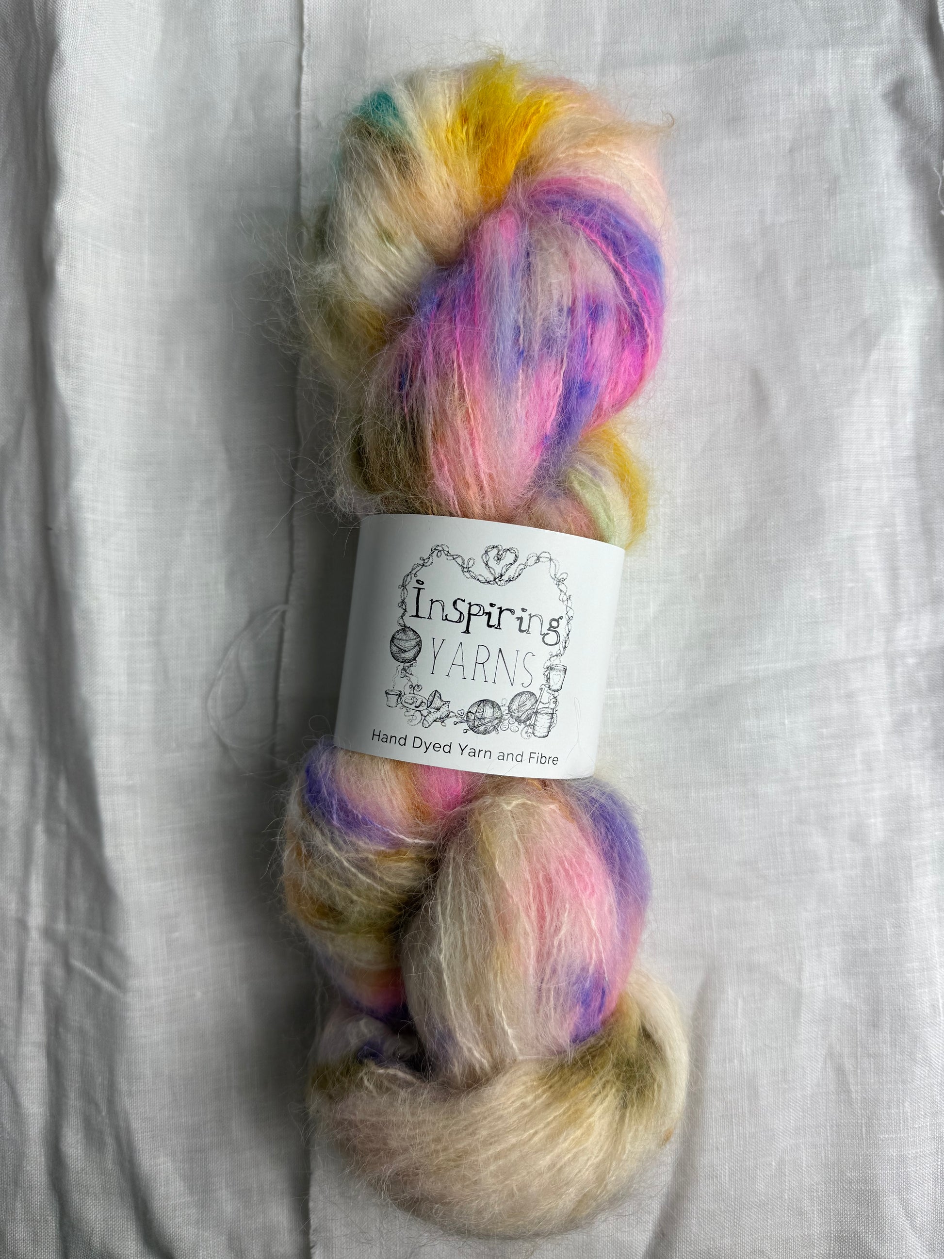 skein of fluffy yarn with natural base and multicoloured speckles with inspiring yarns label on a white background.