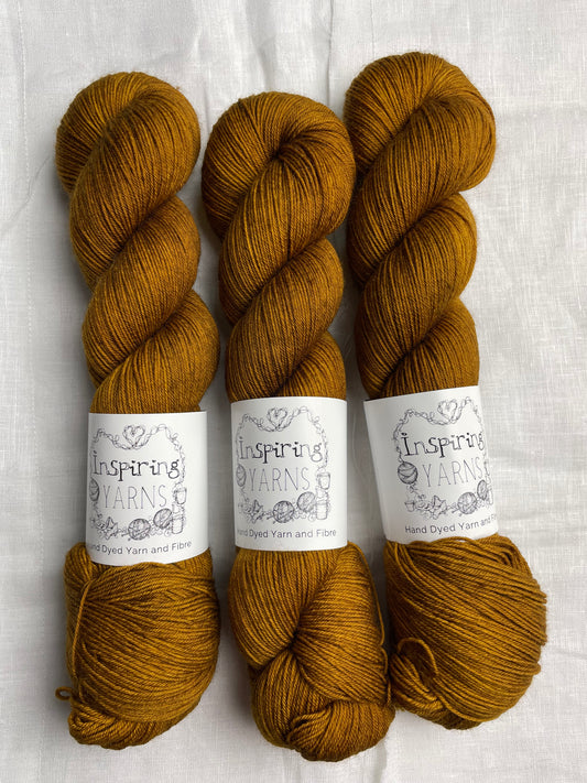 Three tonal toffee brown coloured skeins of Merino Smooth Sock yarn branded  Inspiring Yarns on a white linen fabric background. 