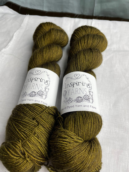 Two tonal dark olive green coloured skeins of hand dyed Yak Silk 4Ply yarn branded Inspiring Yarns on a white linen background.