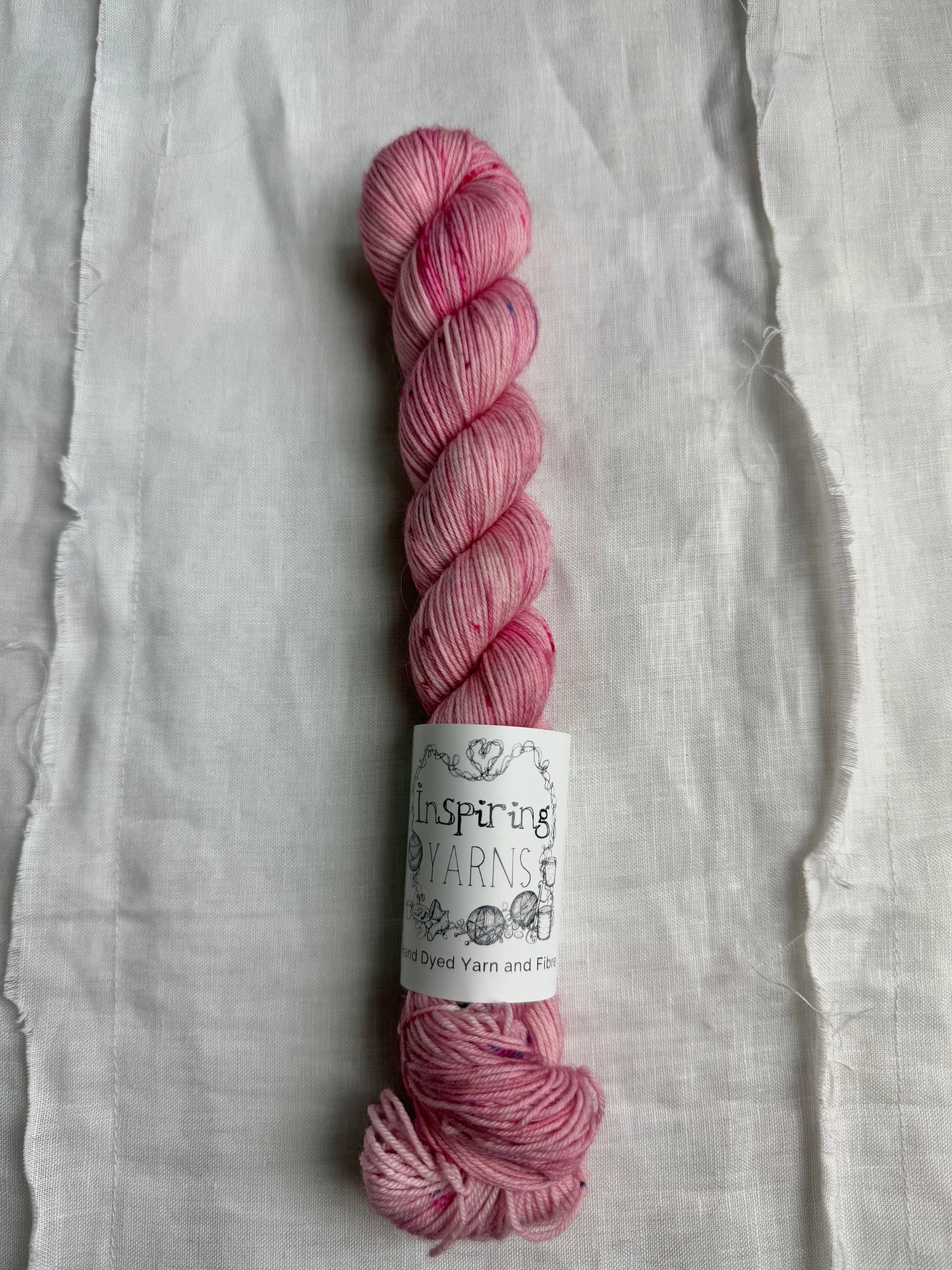 skein of light dusty pink yarn with coloured speckles and an inspiring yarns label on a white background.