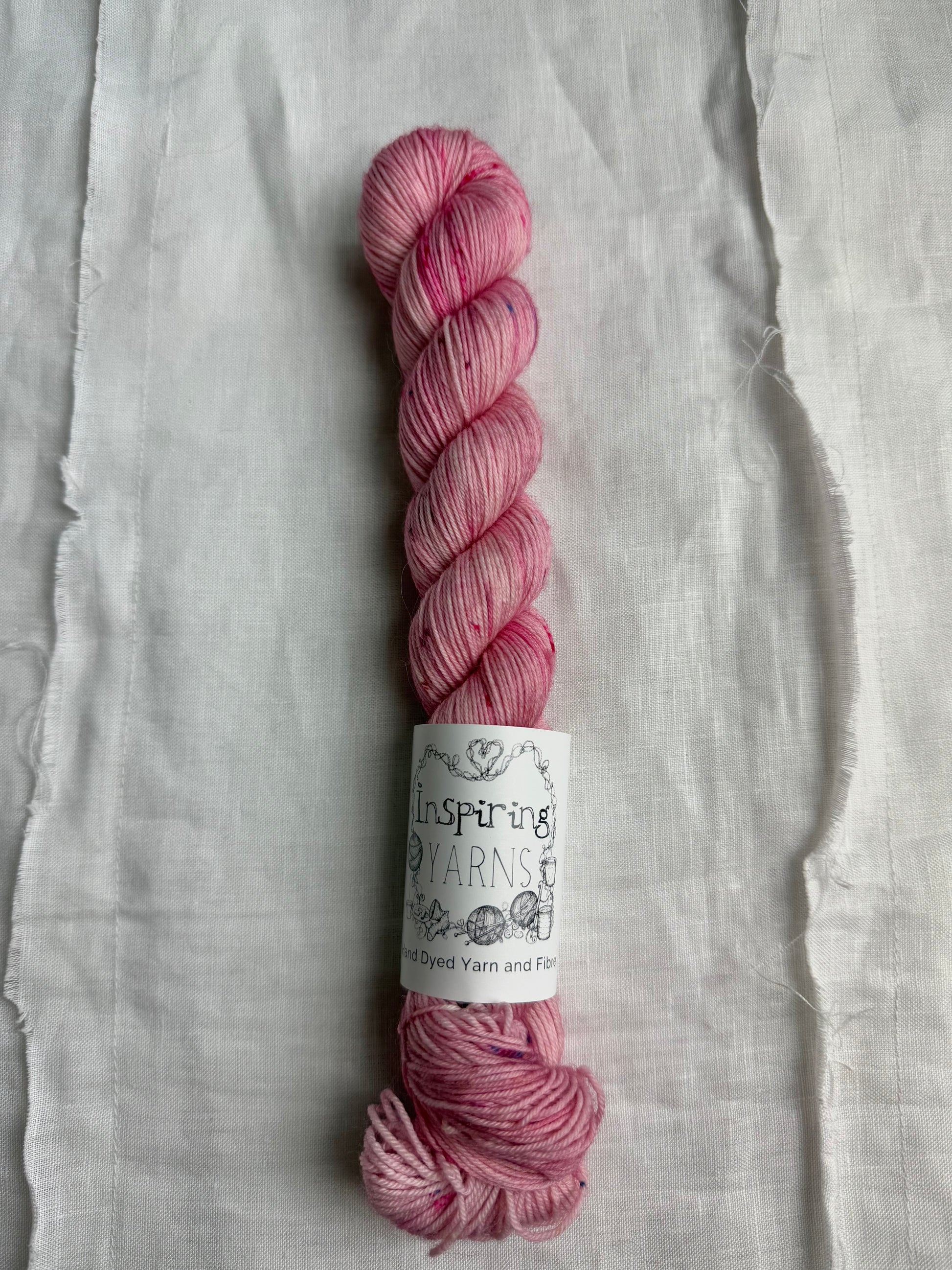 skein of light dusty pink yarn with coloured speckles and an inspiring yarns label on a white background.