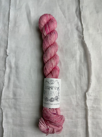 skein of light dusty pink yarn with coloured speckles and an inspiring yarns label on a white background.