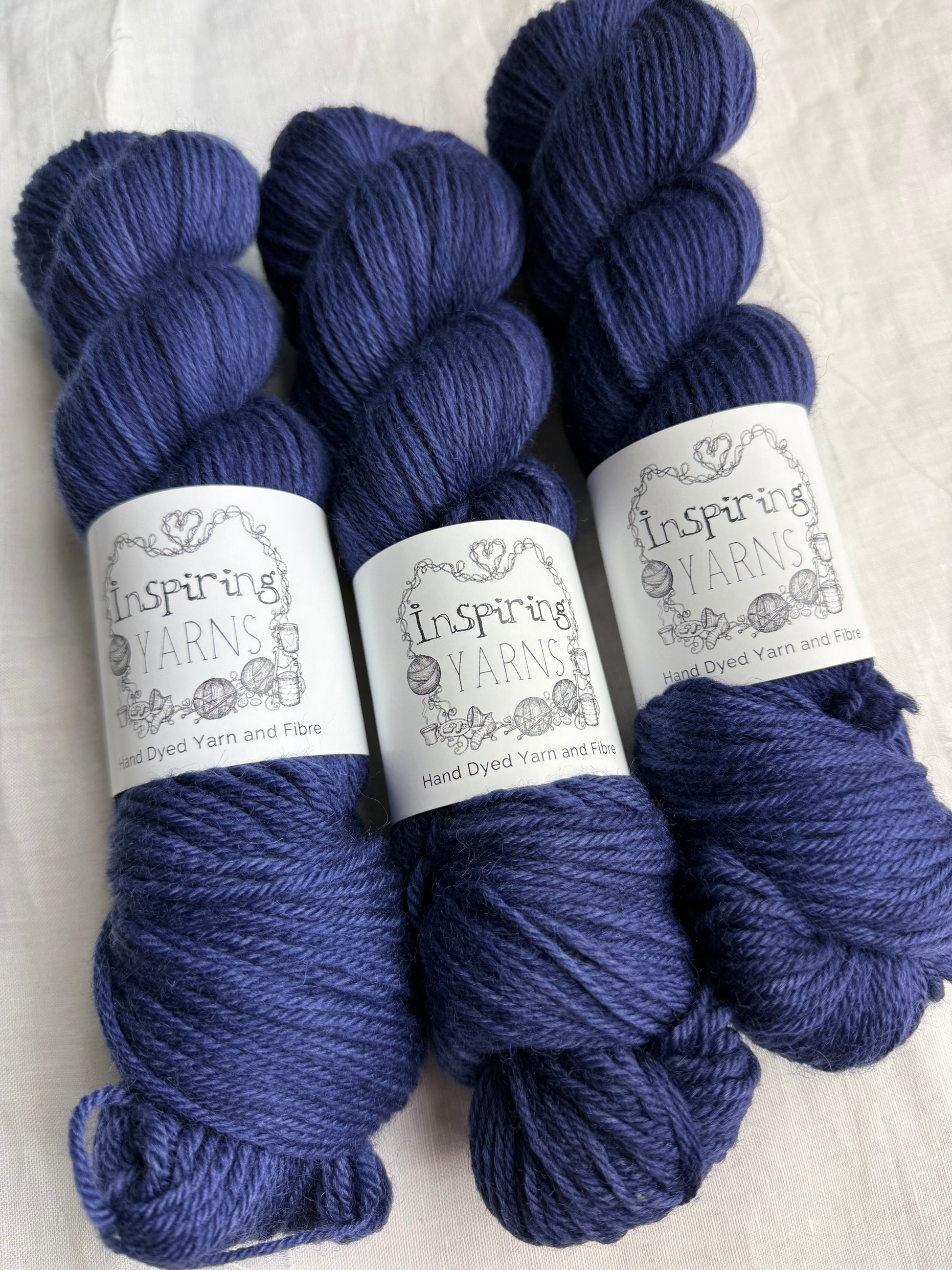Three skeins of dark navy tonal yarn labelled Inspiring Yarns on a white background