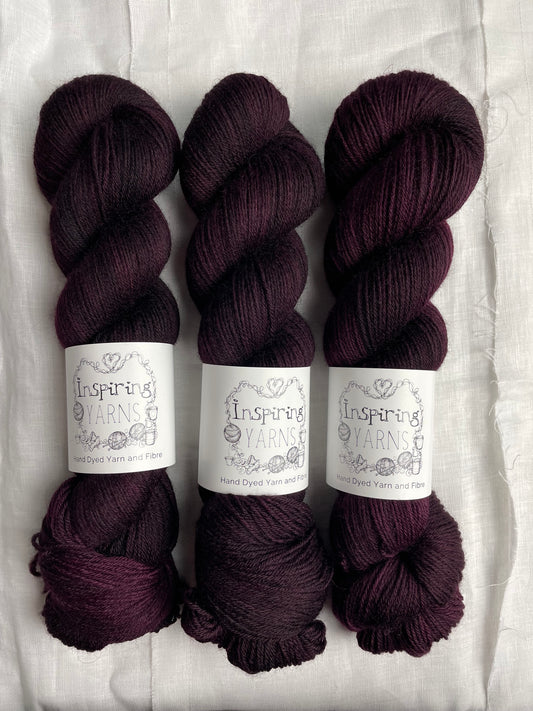 Three skeins of dark burgundy coloured Highland 4Ply labelled Inspiring Yarns on a white linen background.