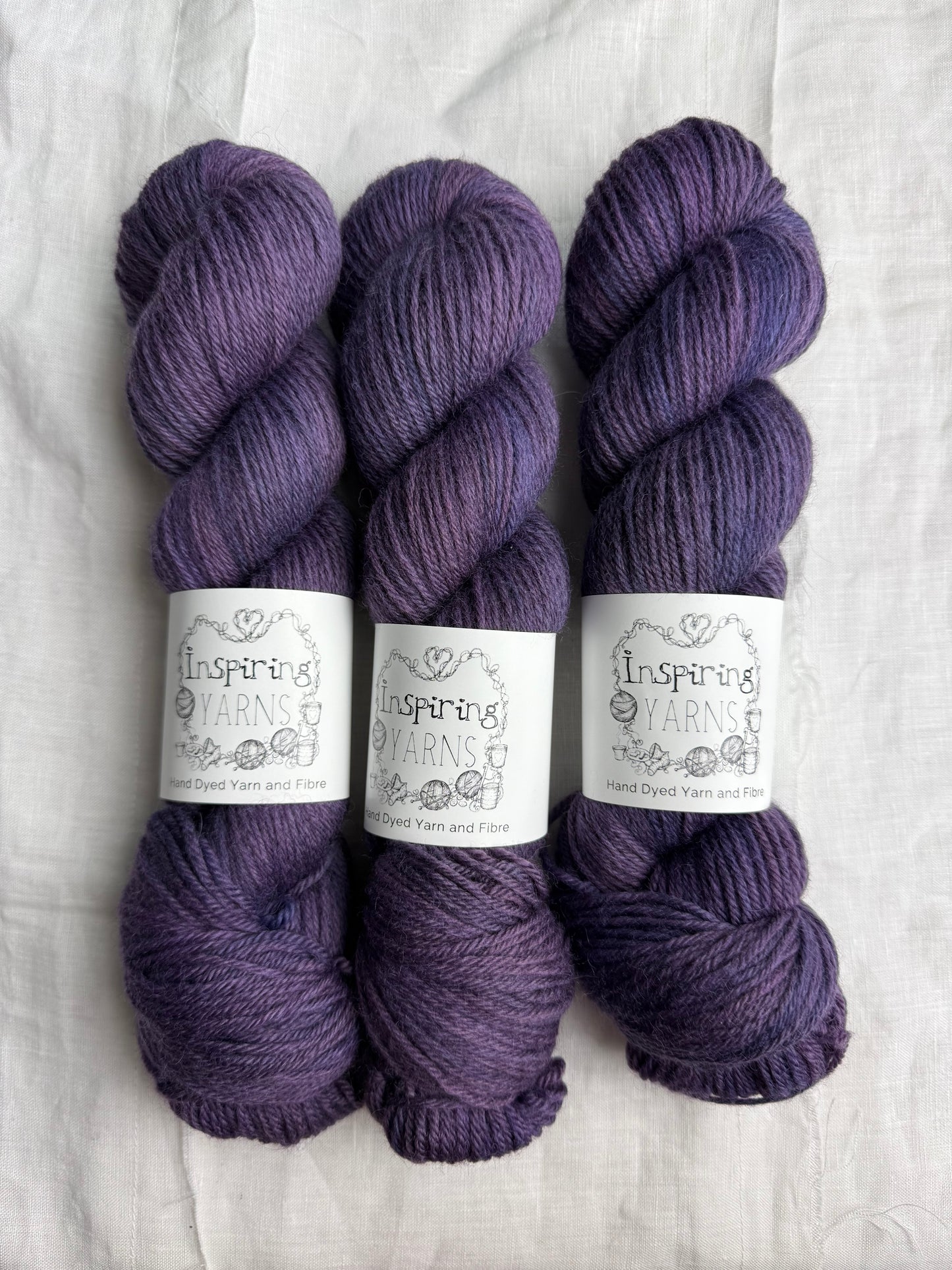 Three skeins of purple tonal yarn labelled Inspiring Yarns on a white background