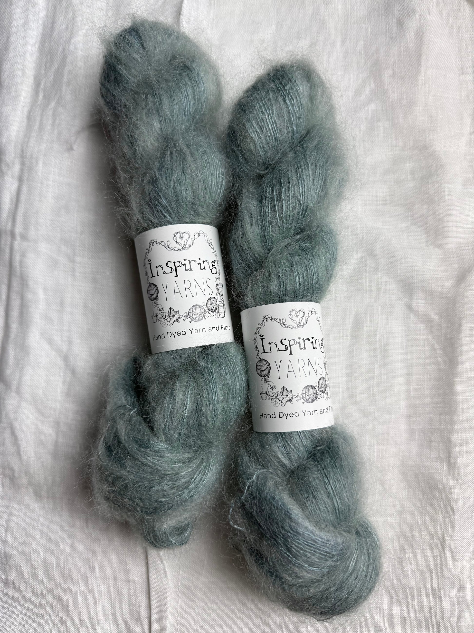 Two skeins of teal coloured mohair silk yarn with 'Inspiring Yarns' labels on a white fabric background