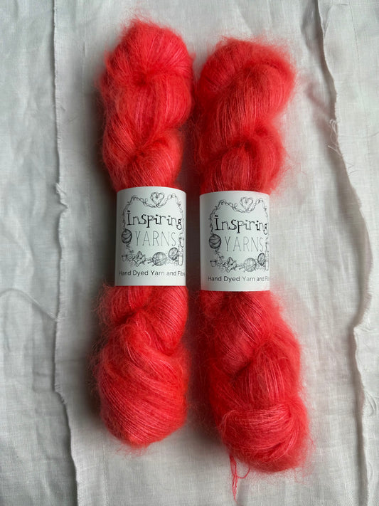two skeins of fluffy mohair yarn in a deep neon coral on a white background and inspiring yarns labels around them.