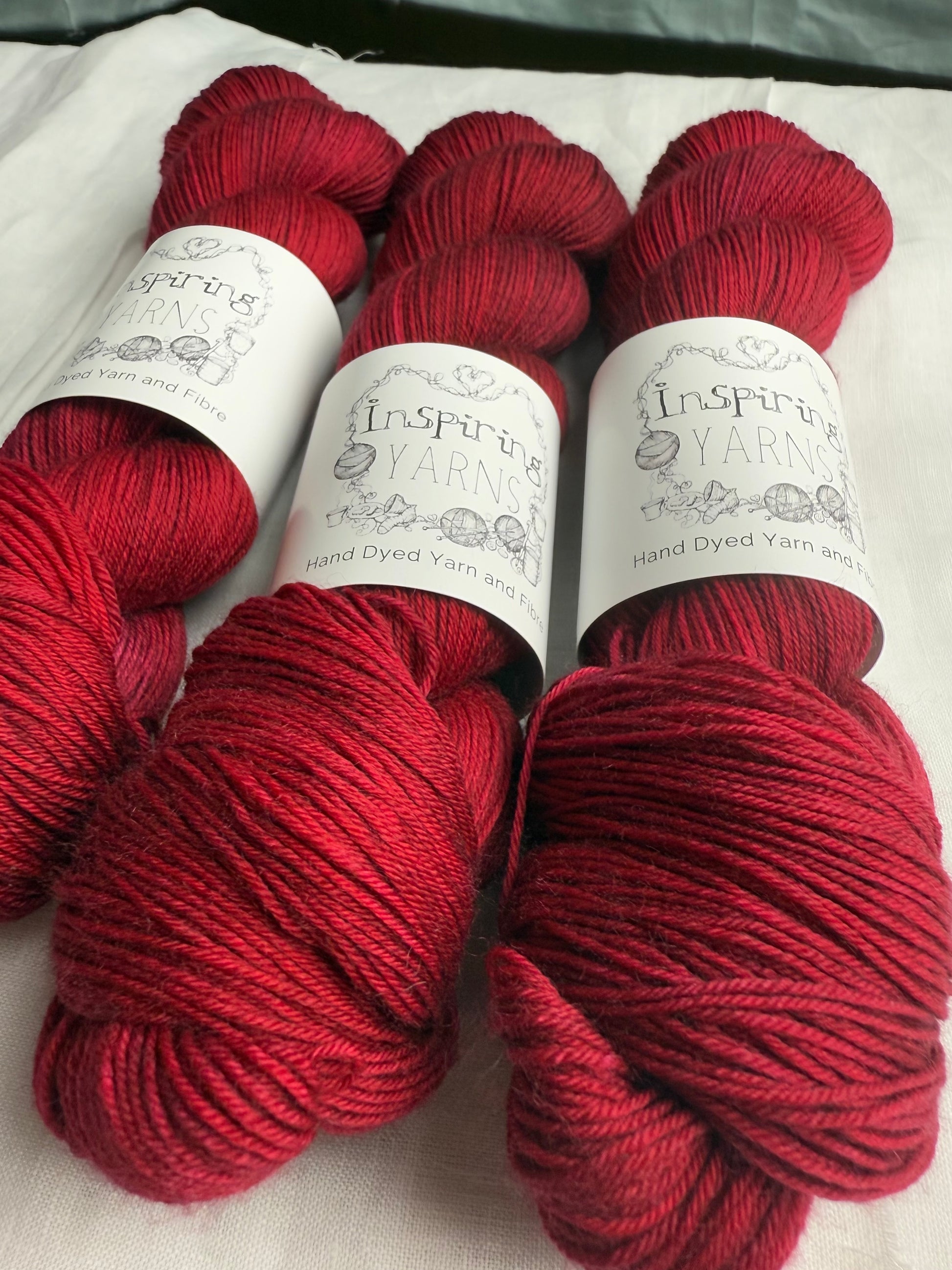 up close of 3 skeins of dark ruby red yarn on white background with inspiring yarns labels.