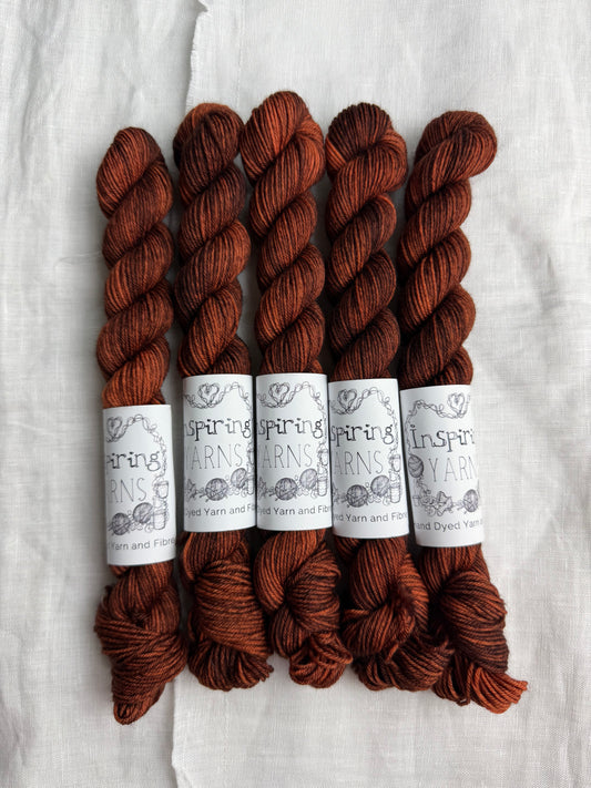 Five skeins of tonal warm brown with orange undertones yarn with Inspiring Yarns labels on a light textured background.