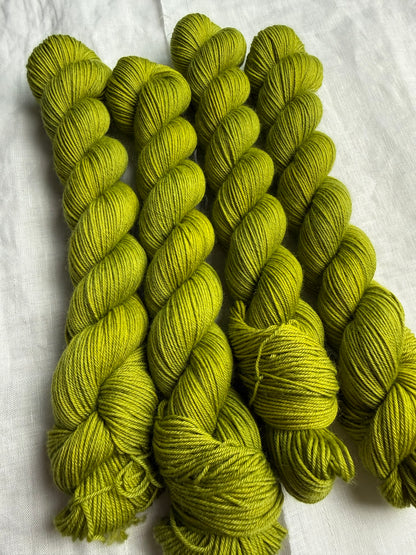 four skeins of bright green hand dyed yarn on a white linen background