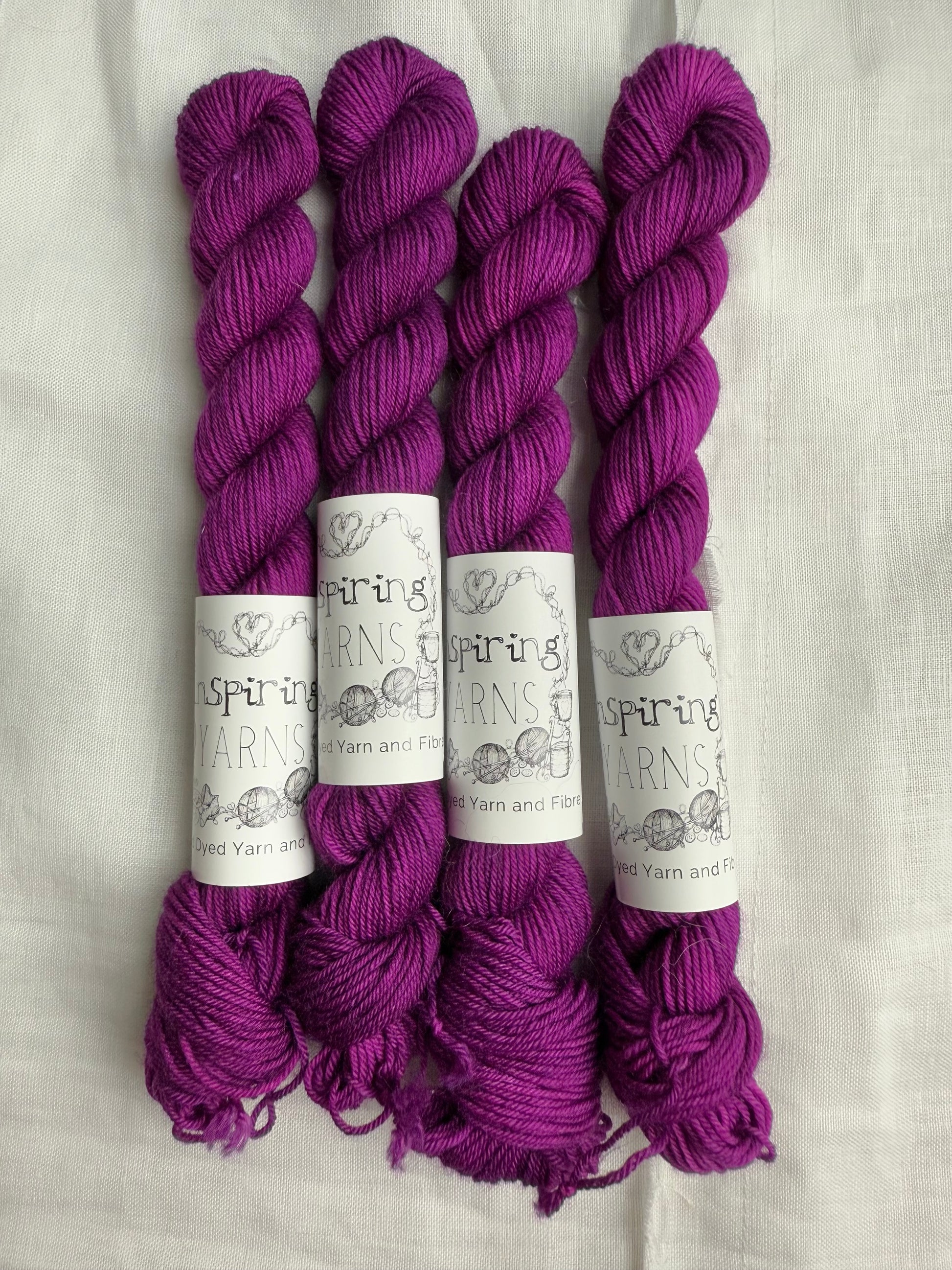 4 mini skeins of tonal fuchsia pink with inspiring yarns labels on a white background.